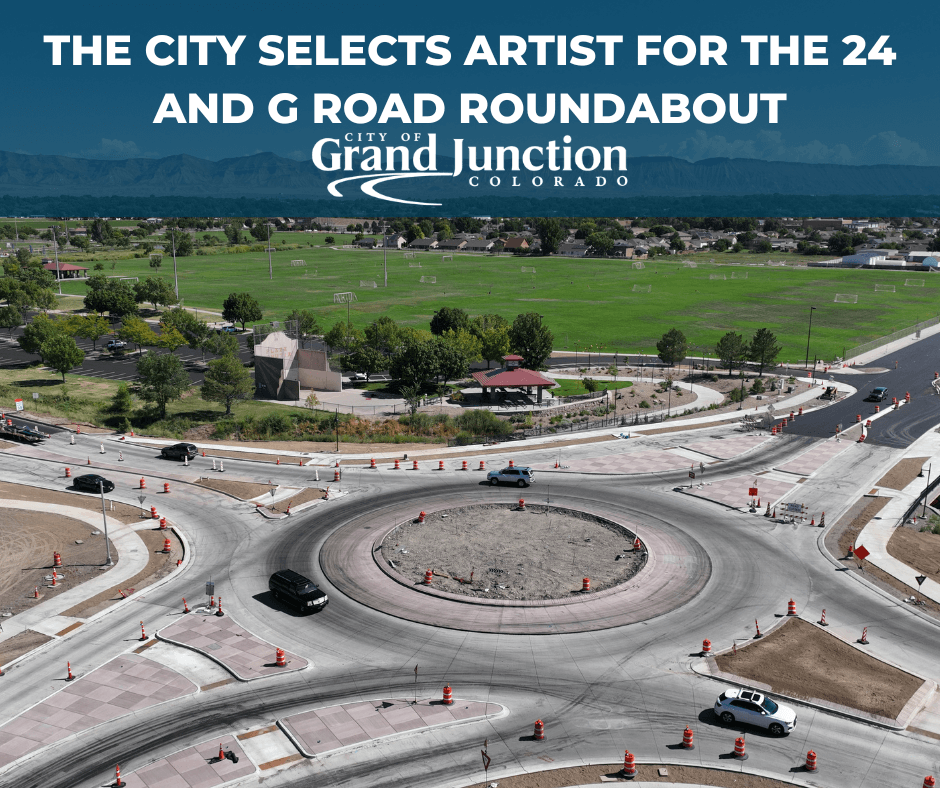 A roundabout with cars driving near a large field. 