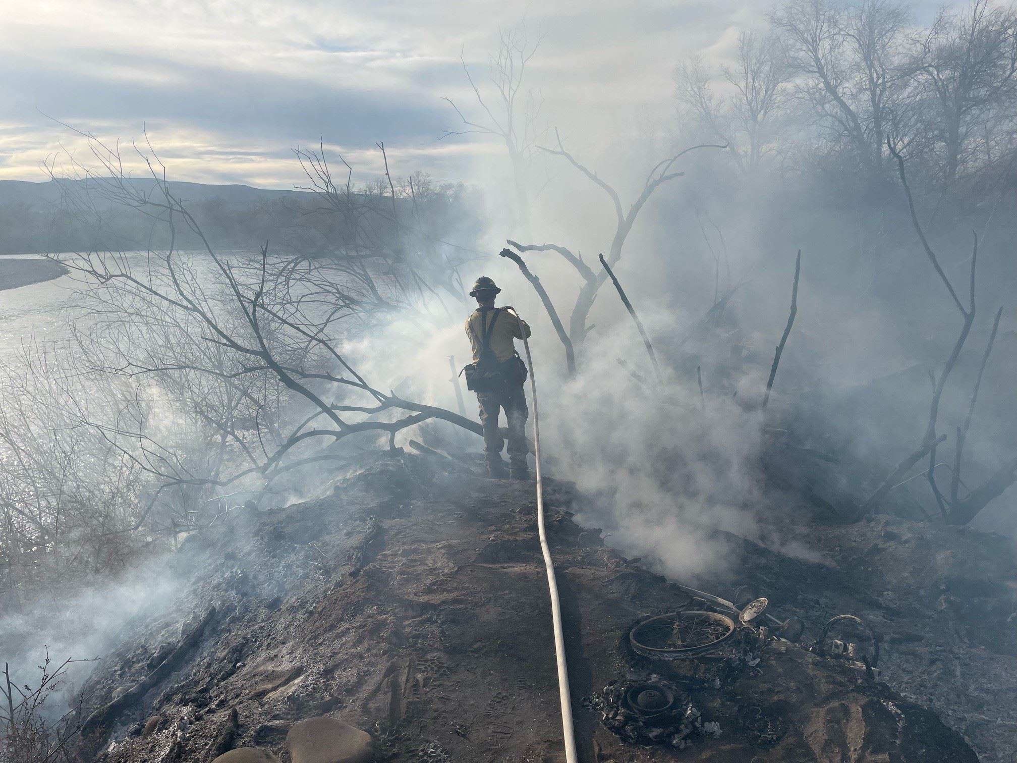 A firefighter by a river, surrounded by smoke.