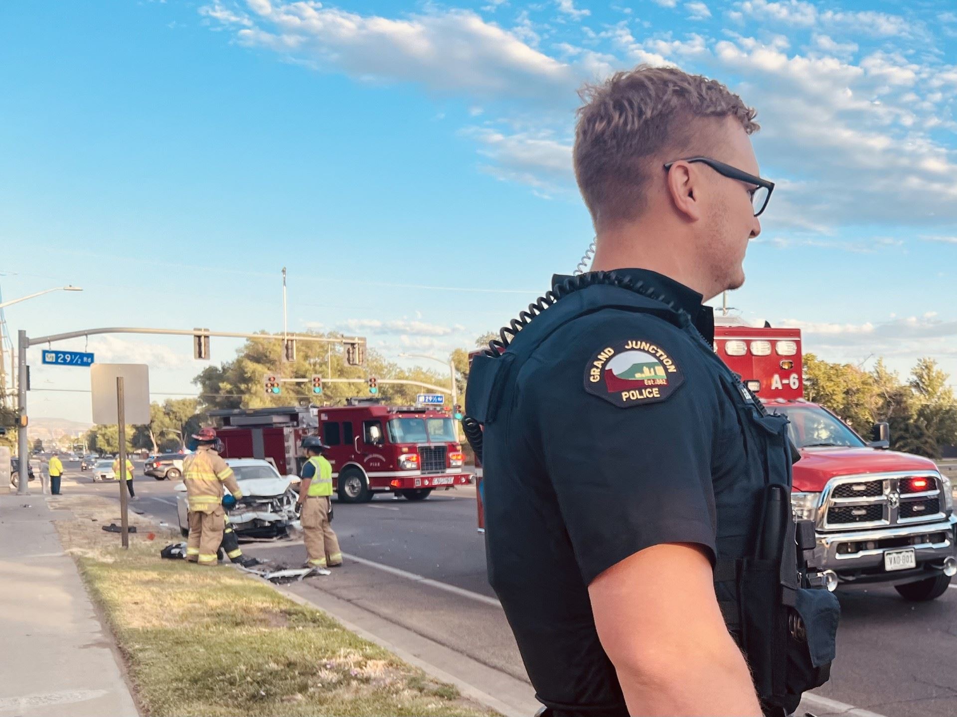 Photo of an officer in the foreground of a crash with fire trucks in the background.