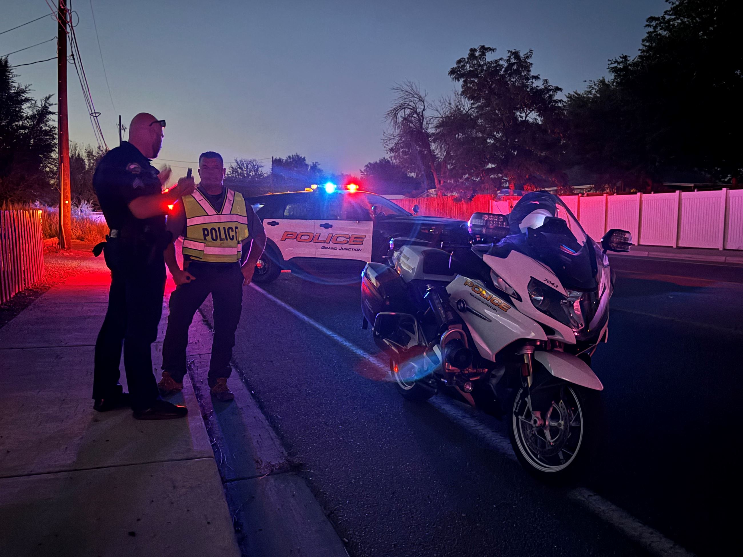 GJPD officers talking at nighttime next to their patrol car and patrol motorcycle on roadway